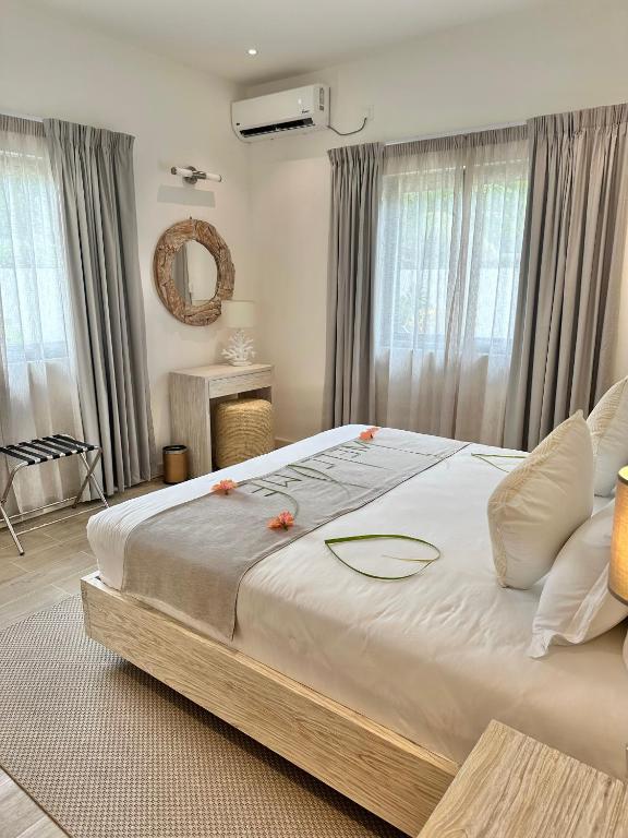 Mūsdienīga guļamistaba ar gaišiem toņiem, liela gulta, eleganta dekora elementi un dabiska apgaismojuma. Logi ar aizkariem nodrošina komfortablu atmosfēru.