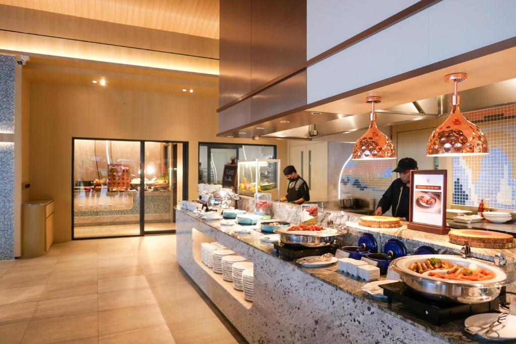 Moderns restorāns ar bufetes stilu, kurā redzami vairāki ēdieni un profesionāli pavāri, kas strādā. Interjers ir elegants, ar modernām lampām un akmens virsmām.