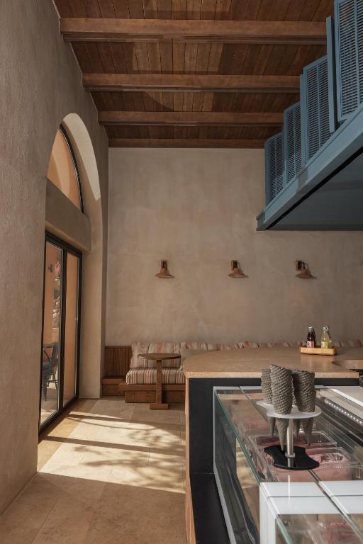 Mūsdienīga interjera dizaina telpa ar koka griestiem un gaišām sienām, kurā redzama sēdvieta un ledusskapis ar saldējuma konusēm. Gaismas elementi pie sienām piešķir siltu atmosfēru.