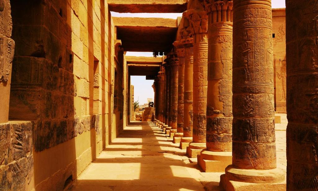 Senās ēģiptes templis ar izteiktām kolonnām un akmens sienām, kas atspoguļo vēsturisko arhitektūru. Dziļa gaisma un ēnas rada noslēpumainu atmosfēru.