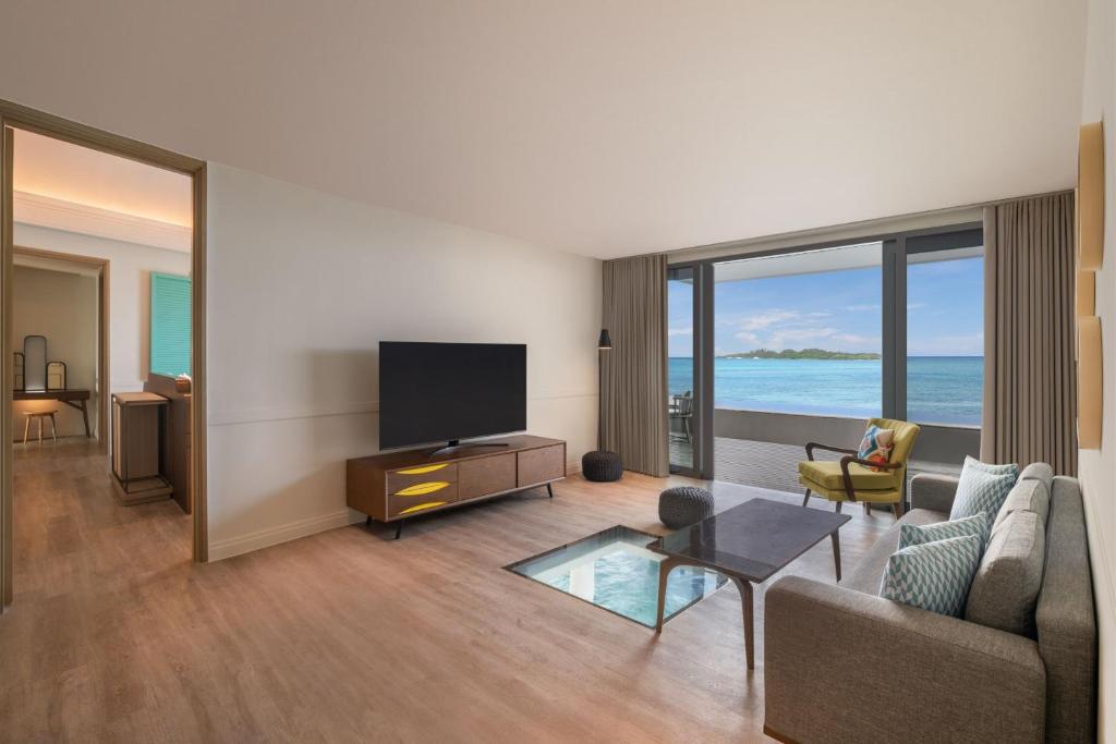 Mūsdienīgs viesistabas interjers ar skatu uz jūru, kurā ir televizors, dīvāns un ērtas krēsls. Lielie logi nodrošina dabīgu apgaismojumu un brīnišķīgu skatu uz ainavu.