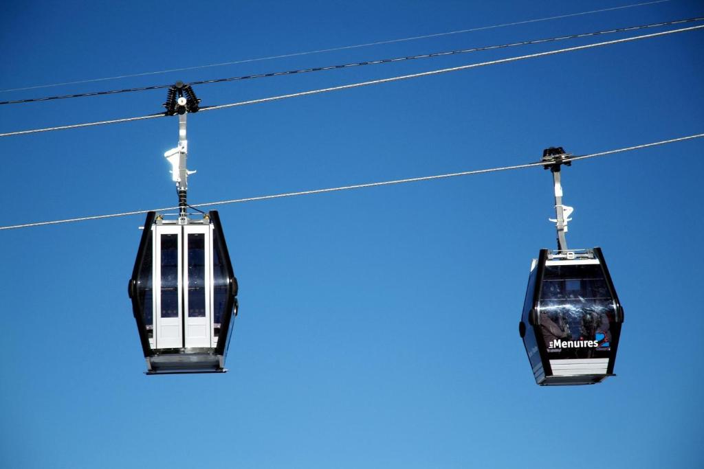 Gaisa tramvajs, kas pārvietojas pa stieplēm, skaidrā zilas debesis fonā.