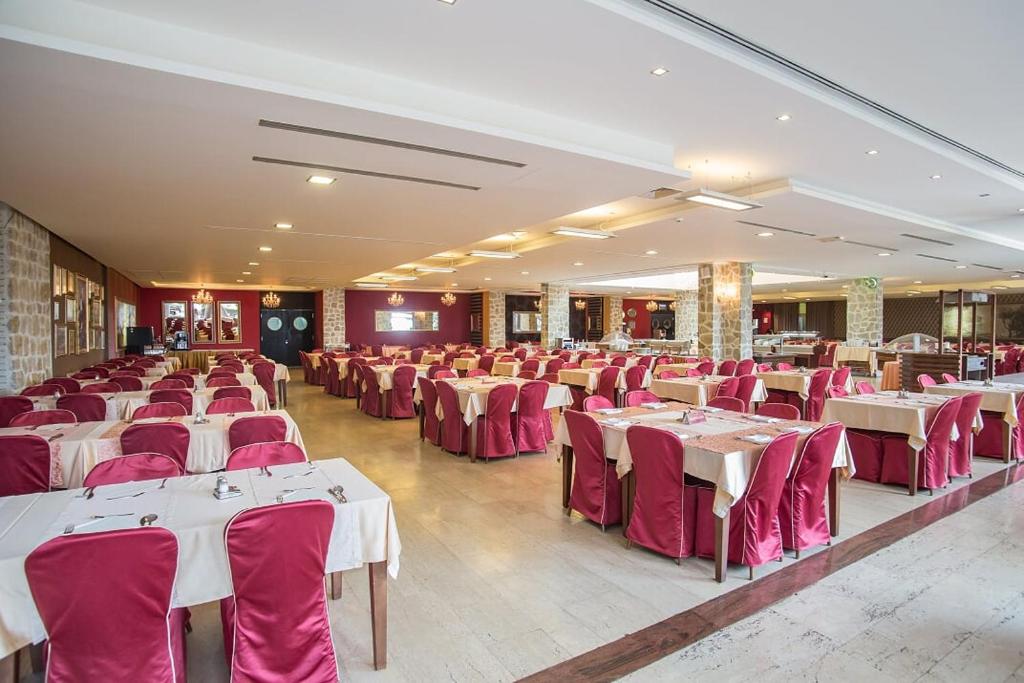 Restorāna iekšskats ar elegantiem galdiem un sarkaniem krēsliem, kas izkārtoti plašā telpā. Gaismas un dizains rada viesmīlīgu atmosfēru.