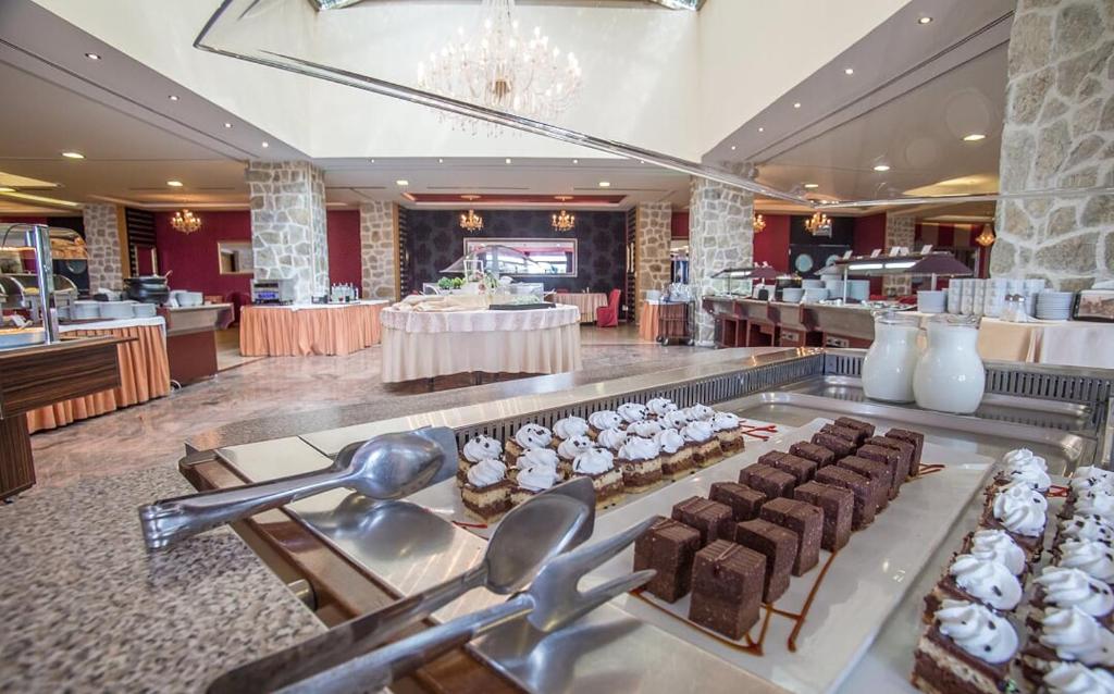 Brokastu bufete ar dažādām kūkām un desertiem elegantā restorānā, kur redzamas dekoratīvas lampas un akmens sienas.