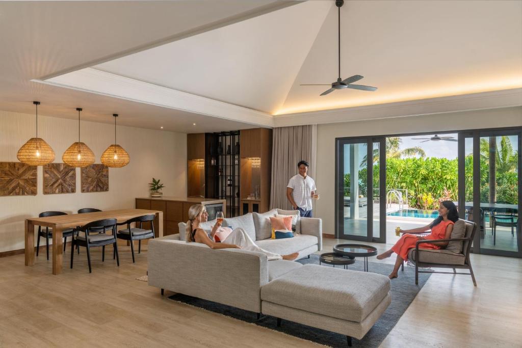 Mūsdienīgs viesistabas interjers ar plašu telpu, kurā redzami cilvēki, kas atpūšas un izbauda dzērienus, ar skatu uz āra baseinu. Svaigas krāsas un dabīgi materiāli rada relaksējošu atmosfēru.