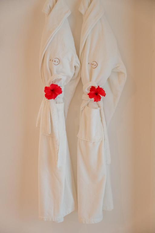 Divi baltie halāti ar sarkanām hibiska ziedu dekorācijām, piekārti pie sienas. Ideāli piemēroti relaksācijai un komfortam.