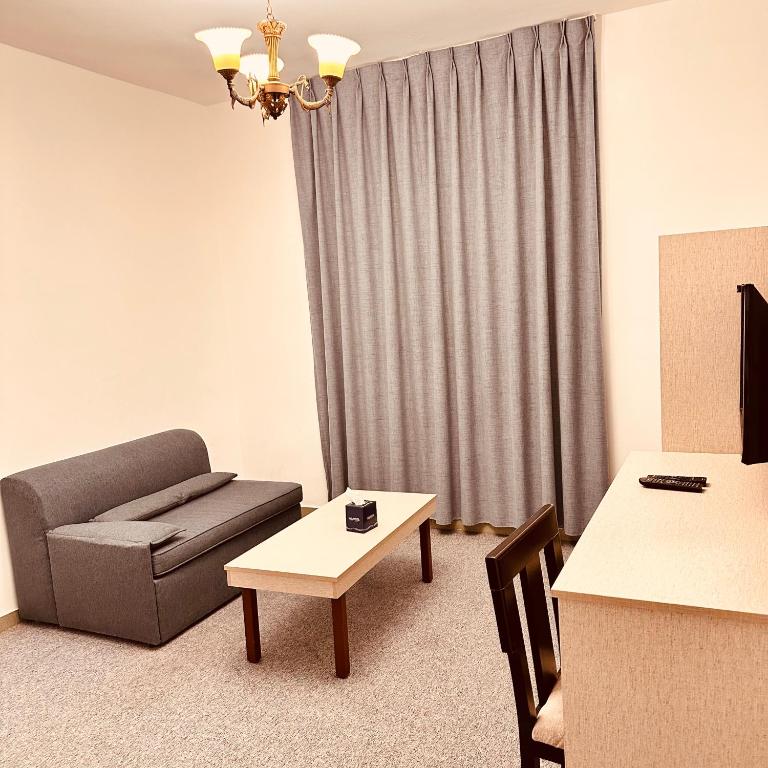 Mūsdienīga viesnīcas numura interjers ar pelēku dīvānu, koka galdu un televizoru. Telpā ir gaismas ķermenis un drapērijas, radot mājīgu atmosfēru.