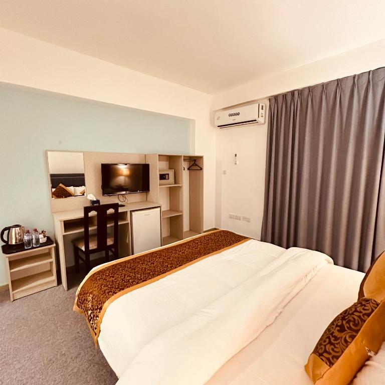 Mūsdienīga viesnīcas numura interjers ar ērtu gultu, televizoru, rakstāmgaldu un mini ledusskapi. Telpa ir gaiša un viesmīlīga, ar pelēkām aizkariem un elegantu dekori.