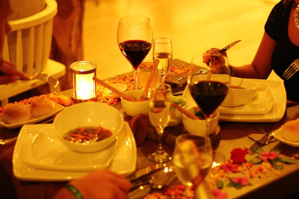 Eleganta vakariņu galda kompozīcija ar siltām maizītēm, vīnu un ziedlapiņām, radot intīmu atmosfēru.