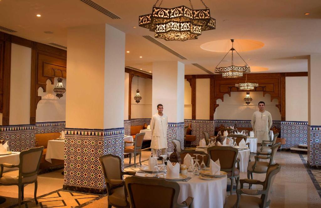 Elegants restorāns ar tradicionālo interjeru, kurā redzami viesmīļi un dekoratīvi elementi. Gaismas lustri un flīžu dekori piešķir patīkamu atmosfēru.
