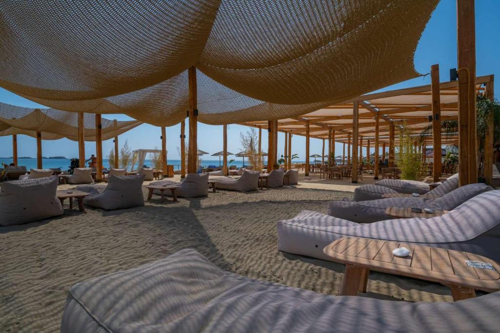 Pludmales atpūtas zona ar ērtām gultām un saules sargiem, kas nodrošina ēnu. Apkārt ir koka konstrukcijas un augu akcenti, radot relaksējošu atmosfēru pie jūras.