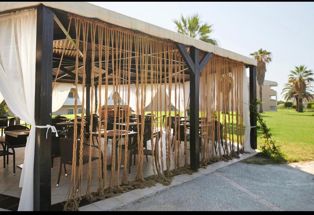 Āra restorāna nojume ar dabīgiem materiāliem, sēdvietām un saulainu skatu uz zālienu. Dabas elementi un stilīgs dizains rada relaksējošu atmosfēru.