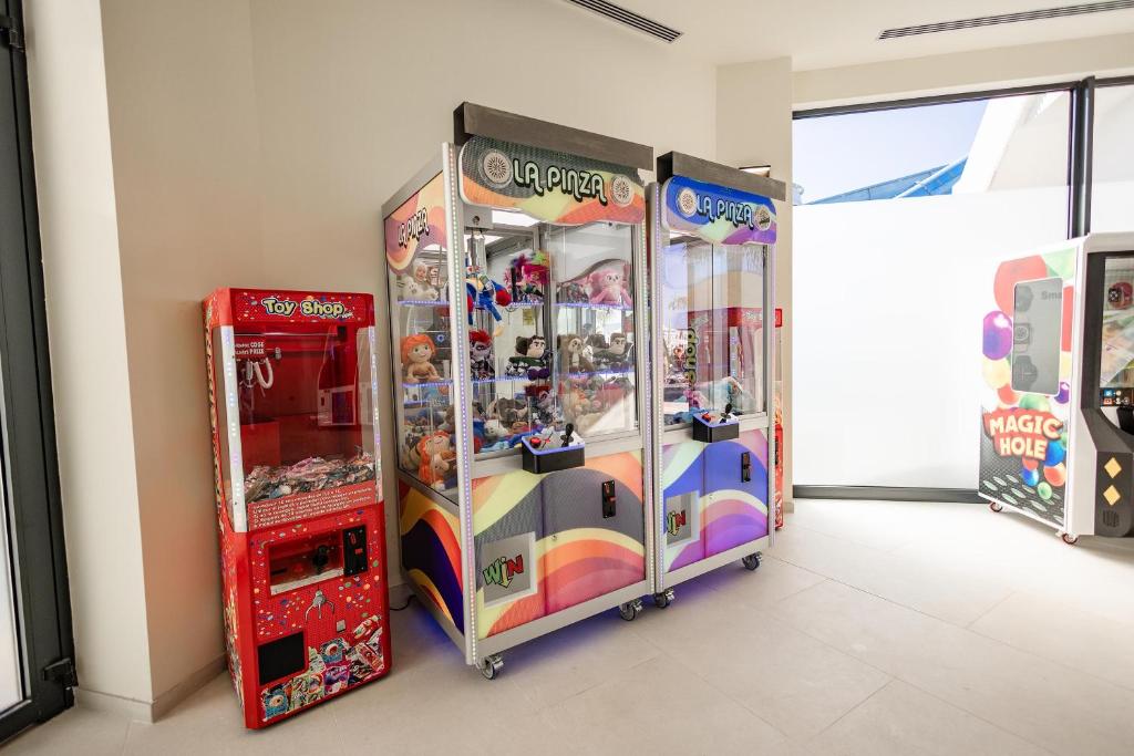 Spēļu automāti ar leļļu un rotaļlietu izsniegšanu, ieskaitot "Toy Shop" un "La Pinza", atrodas gaišā telpā.