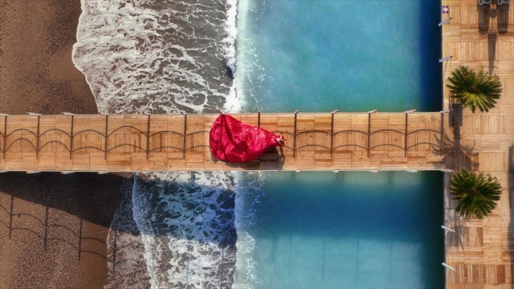 Sarkana kleita uz koka piestātves, kas atrodas starp divām ūdens virsmām, ar viļņiem krastā.