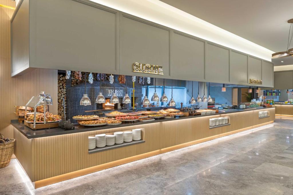 Mūsdienīgs bufetes galdiņš ar plašu ēdienu klāstu, ieskaitot dažādas uzkodas un galvenos ēdienus, izgaismots ar stilīgām lampām un dekoratīviem elementiem.