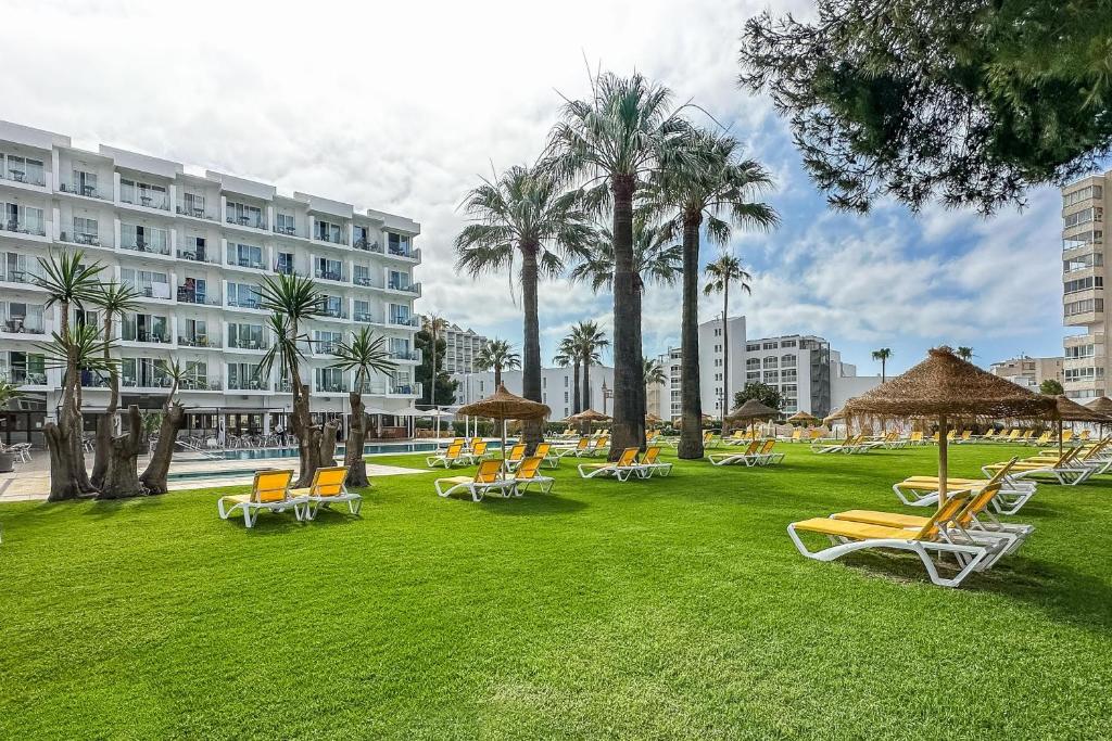 Vasaras kūrorta ainava ar zālienu, baseinu un saulessargiem, apkārt palmām un viesnīcas ēku. Ideāla vieta relaksācijai un atpūtai.