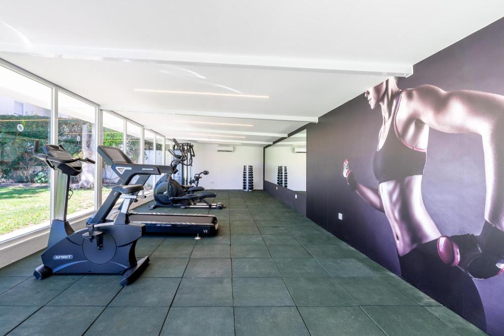 Mūsdienīga sporta zāle ar skaidru dizainu, aprīkota ar trenažieriem un svaru plauktiem. Sienā ir liela fotogrāfija, kas iedvesmo aktīvu dzīvesveidu.