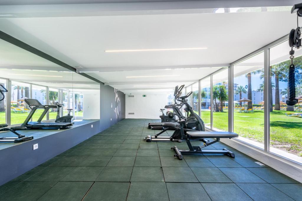 Mūsdienīga sporta zāle ar plašiem logiem un skatu uz dārzu, aprīkota ar dažādām trenažieriem un gumijas grīdu. Ideāla vieta fiziskām aktivitātēm un veselīga dzīvesveida veicināšanai.