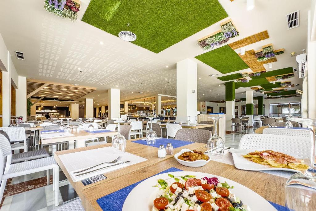 Mūsdienīgs restorāns ar zaļiem dekoriem uz griestiem un elegantām maltītēm uz galda. Telpa ir gaiša un plaša, radot patīkamu atmosfēru.