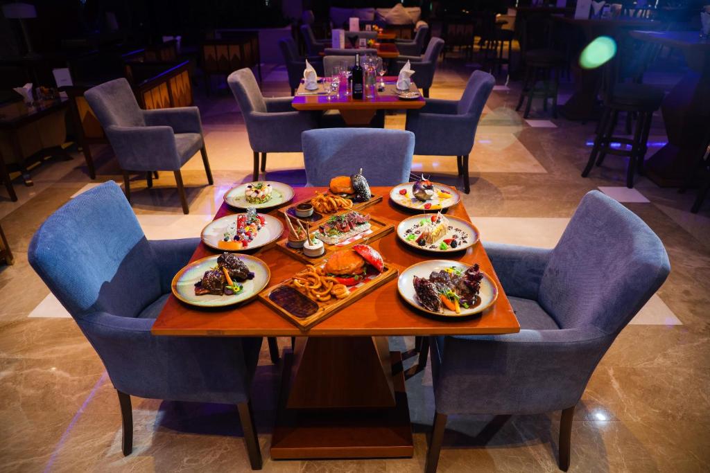 Elegantā restorāna galds ar dažādiem izsmalcinātiem ēdieniem, ieskaitot gaļu un desertus, skaisti noformēts ar mūsdienīgām krēslām. Ideāla vieta gastronomiskai baudai.