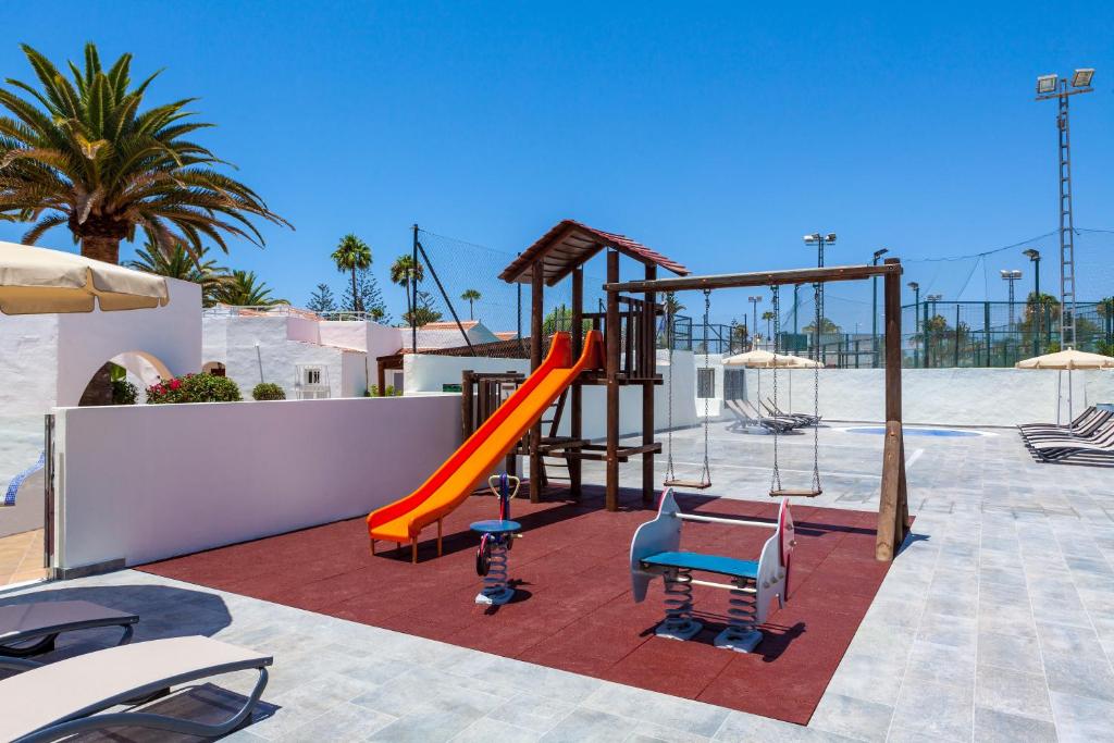 Bērnu rotaļu laukums ar slidkalniņu un šūpolēm, apzaļumots ar palmām, saulains laiks un skaidrs debesis. Ideāli piemērots ģimenēm ar bērniem.