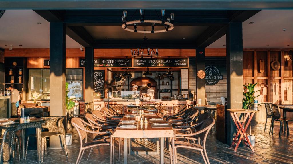 Restorāna interjers ar siltu apgaismojumu un koka mēbelēm, kur redzama atvērta virtuve un picas cepšanas zona. Erotiskā atmosfēra un tropiskais stils rada patīkamu vietu, kur baudīt autentisku picu.