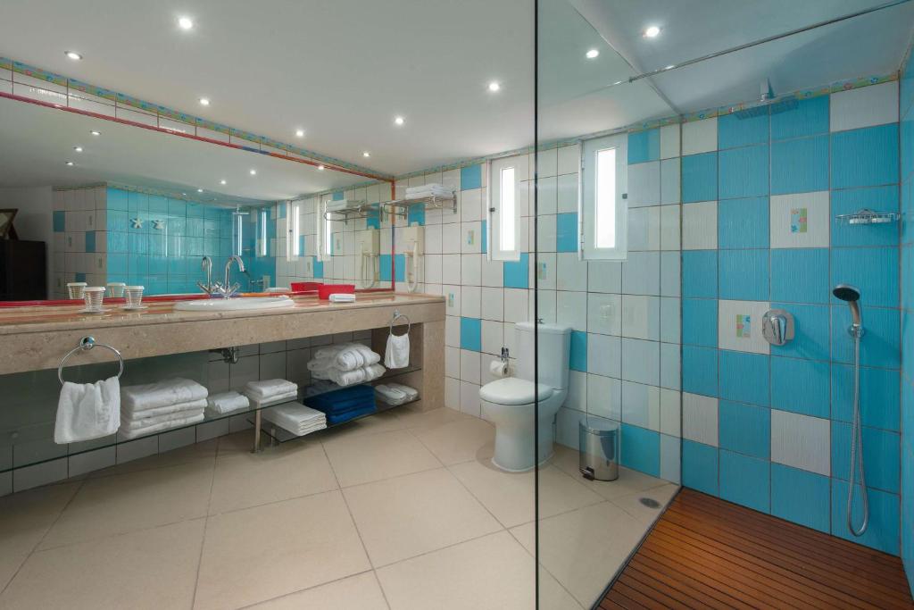 Mūsdienīgs vannas istabas interjers ar zilu un baltu flīžu dizainu, liela spoguļa un eleganta izlietne. Vannas istabā ir arī duša un glabāšanas plaukti ar tīrām dvieļiem.