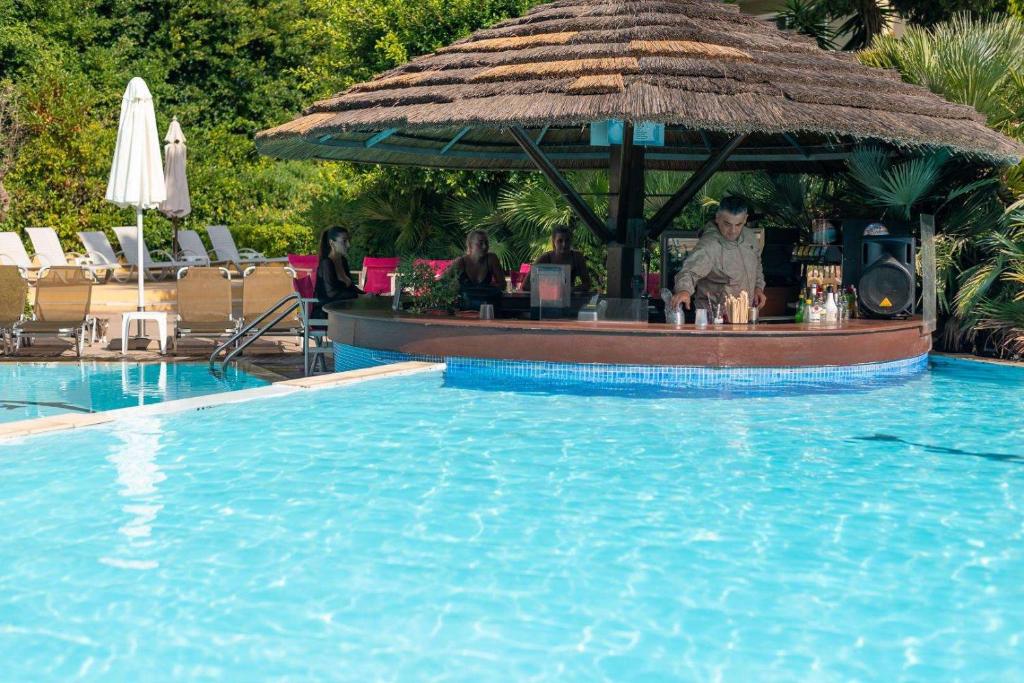 Baseins ar bāru, kurā tiek pasniegti dzērieni, un atpūtnieki, kas bauda sauli. Apkārt ir palmām un sauļošanās krēsliem.