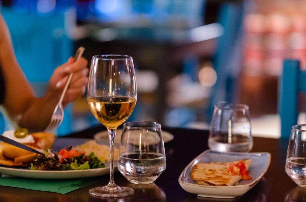 Elegantā vakariņu aina ar vīna glāzi un dažādiem ēdieniem, tostarp salātiem un desertu, intīmā restorāna atmosfērā.