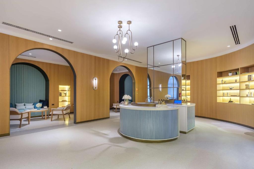 Mūsdienīgs viesnīcas reģistratūras interjers ar koka apdares elementiem, elegantu apgaismojumu un atpūtas zonu. Iekārtojums ir gaišs un stilīgs, radot komfortablu atmosfēru.