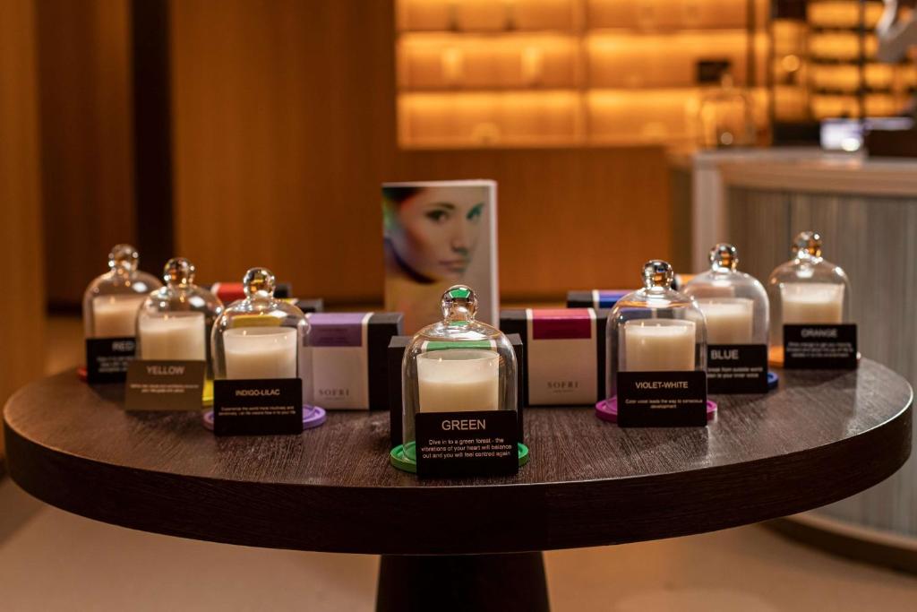 Stilīgu aromātisko sveču kolekcija, kas izvietota uz koka galda, katra svece ir pasniegta ar krāsainu vāku un aprakstu. Sveču krāsas ietver sarkanu, dzeltenu, zaļu, indigo, violeto un oranžu.