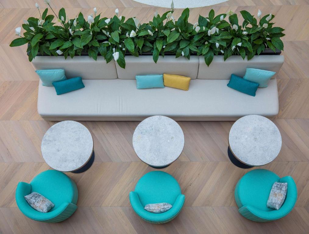 Mūsdienīgs atpūtas stūris ar zaļām augiem, moderna dīvāna un krēslu kombinācija. Gaišas krāsas spilveni un apaļi galdi veido patīkamu atmosfēru.