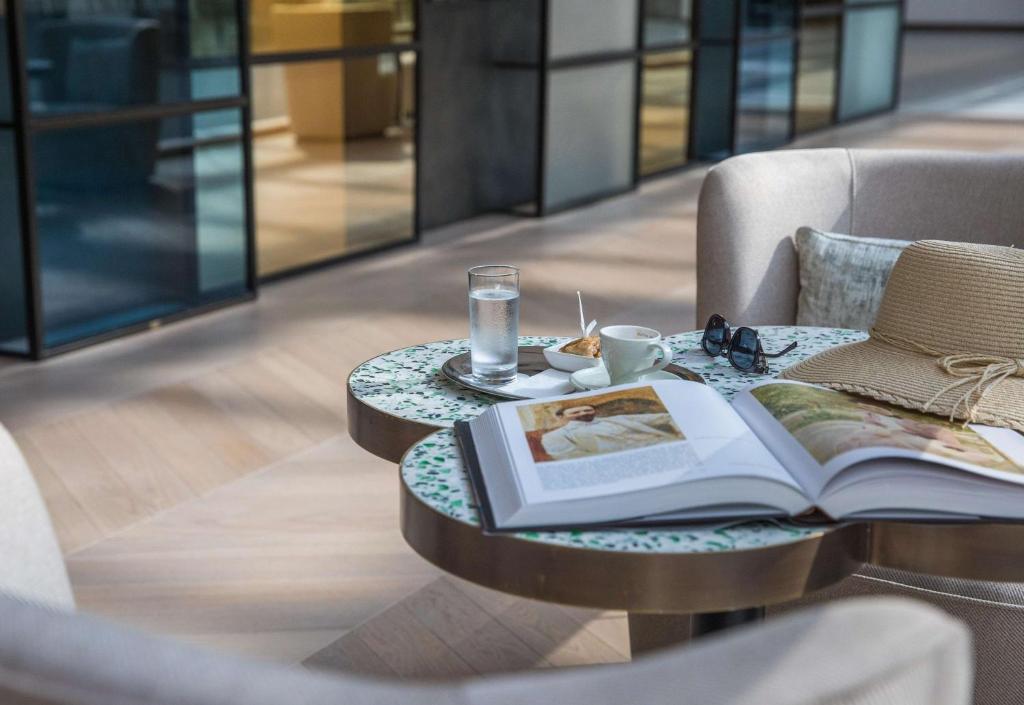 Relaksējošs brīdis ar grāmatu, ūdeni un kafiju uz stilīga galda, blakus cepums, saulesbrilles un tuvojošs pludmales cepure. Ideāla vide atpūtai un izklaidei.