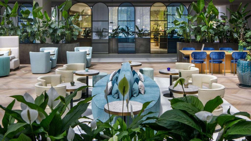 Mūsdienīga viesnīcas vestibila telpa ar augiem un dažādiem sēdvietu risinājumiem, radot relaksējošu atmosfēru. Interjers apvieno gaišas krāsas un stilīgu dizainu.