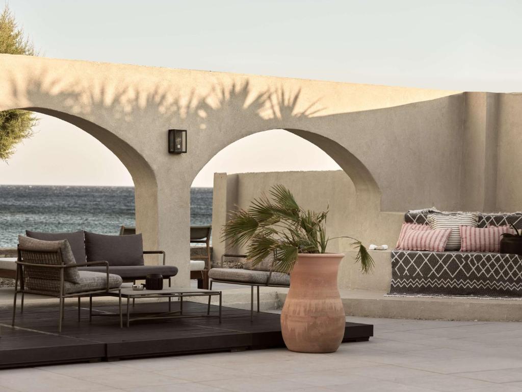 Mūsdienīgs terases dizains ar arku, kurā ir ērti krēsli un dīvāns, kā arī dekoratīva puķu pods ar palmu. Fons veido mierīga jūras ainava.