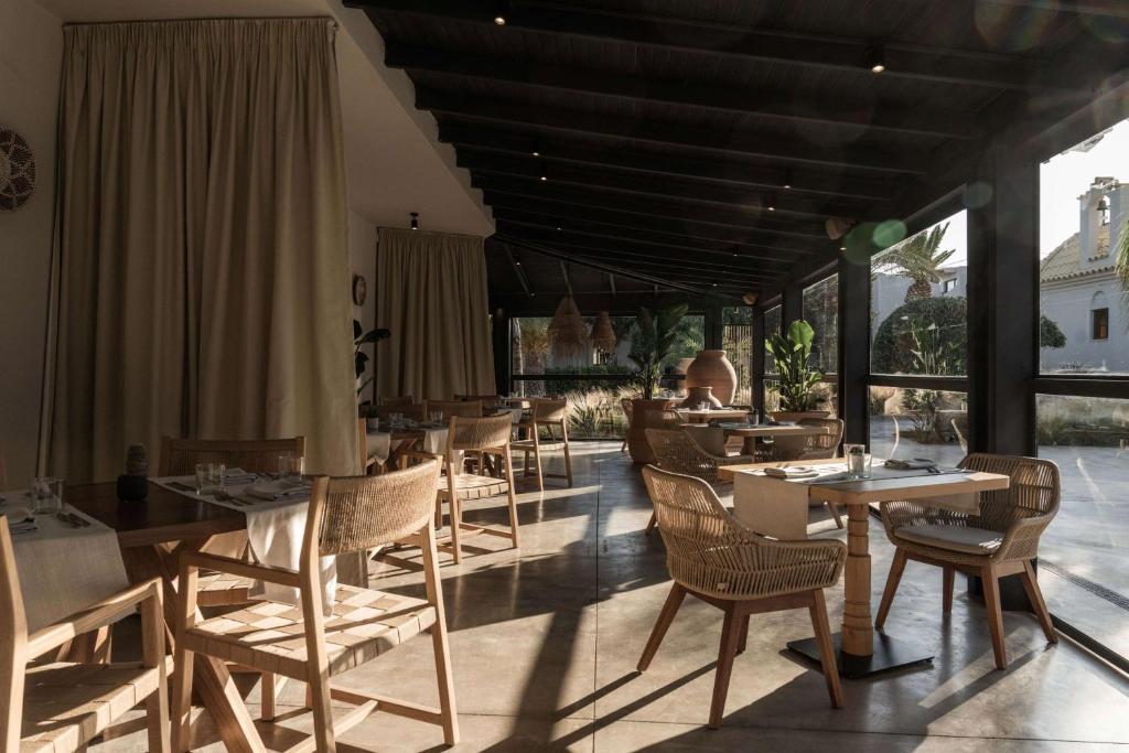 Mūsdienīgs restorāna interjers ar koka mēbelēm un plašiem logiem, kas ļauj ienākt dabiskai gaismai. Telpā ir ērtas krēsli un galdi, radot patīkamu atmosfēru.