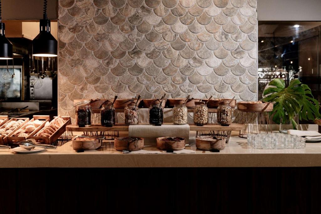 Stilīgs bufete ar dažādiem konditorejas izstrādājumiem un graudaugiem, ko pasniedz uz koka plauktiem, pret elegantu mozaīkas sienu.