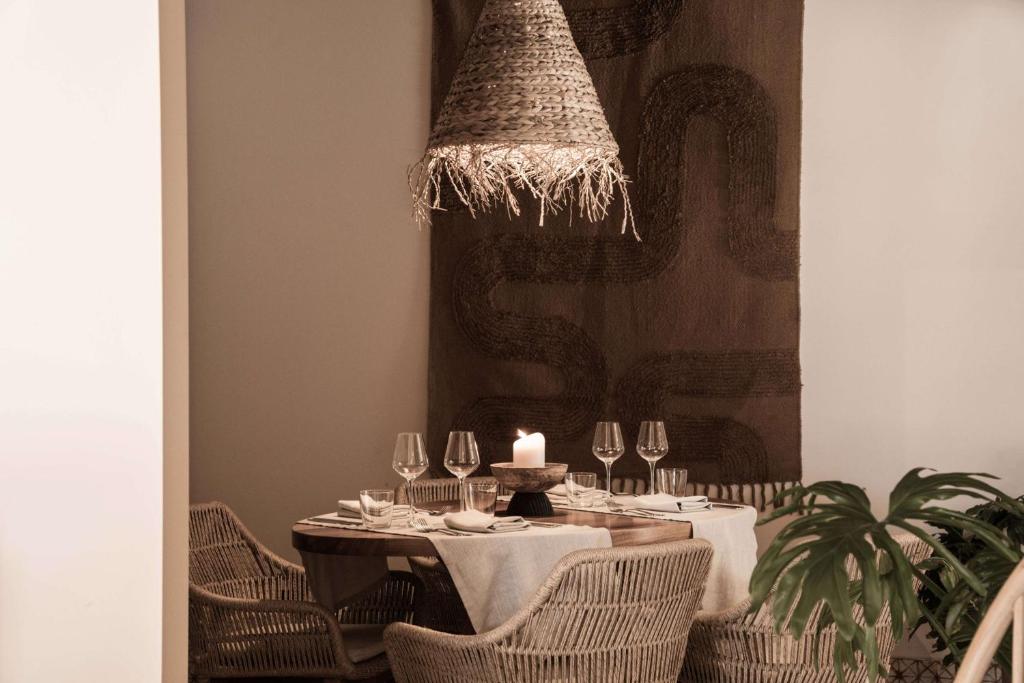 Elegants restorāna interjers ar apaļu galdu, kas klāts ar balto galdautu un sveci vidū. Apkārt galdu ir vīna glāzes un ratiņu krēsli, bet sienā redzama mākslinieciska auduma dekorācija un stilīga virsma.