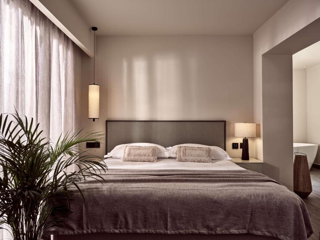 Mūsdienīgs guļamistabas interjers ar ērtu gultu un gaismas avotiem, kas rada siltu atmosfēru. Logi ar caurspīdīgām aizkariem un augu akcenti piešķir telpai dabisku šarmu.