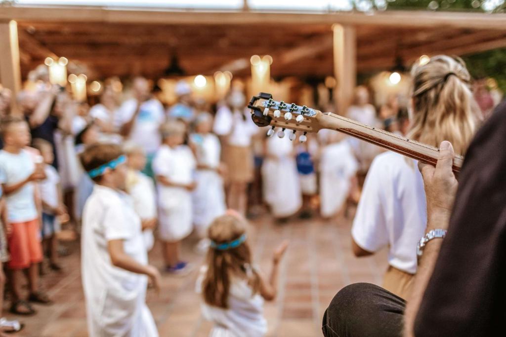 Bērni dejo un izklaidējas pie mūzikas pavadījuma, kamēr viens no dalībniekiem spēlē ģitāru. Pasākums notiek brīvā dabā, apgaismots ar siltām gaismām.