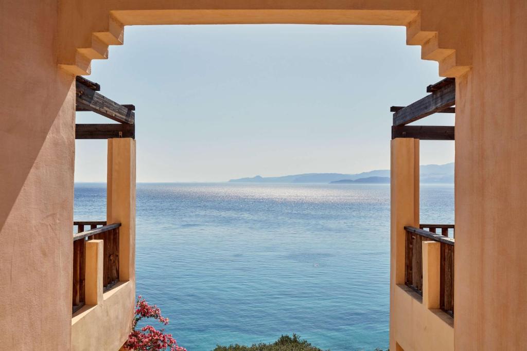 Skats no terases uz jūru, rādot mierīgu ūdeni un kalnu ainavu tālumā, ar ziediem tuvumā.