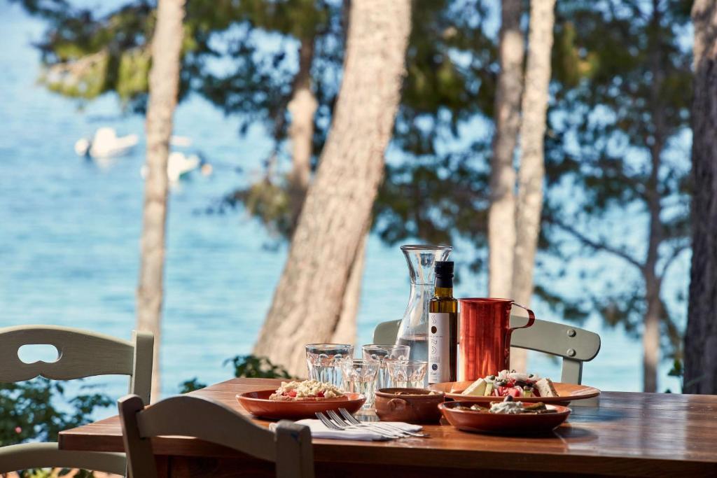 Galda klāšana pie jūras ar salātiem un dzērieniem, apkārt augoši koki un mierīgs ūdens. Ideāls brīdis atpūtai un baudīšanai.