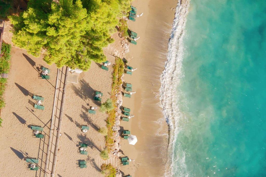 Pludmales skats no augšas ar saulessargiem un sauļošanās krēsliem, gaiši smilšaini krasti un kristāldzidrs ūdens.