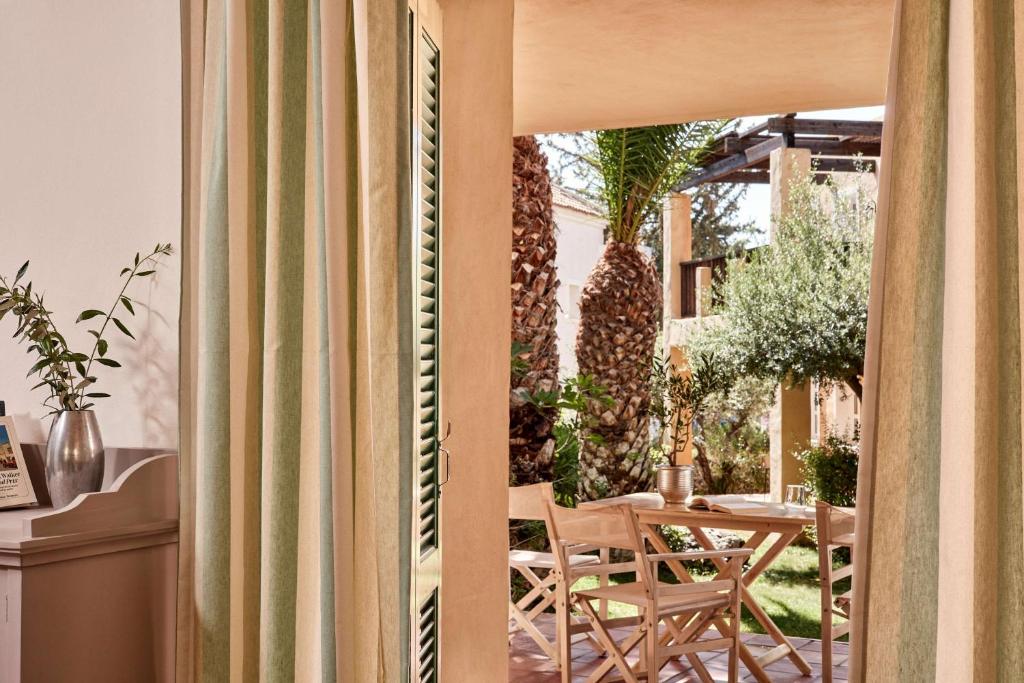 Gaismas istaba ar zaļām svītrām, kas atveras uz elegantu āra terasi, kur atrodas koka galds un krēsli, apkārt augošiem palmām un augiem.