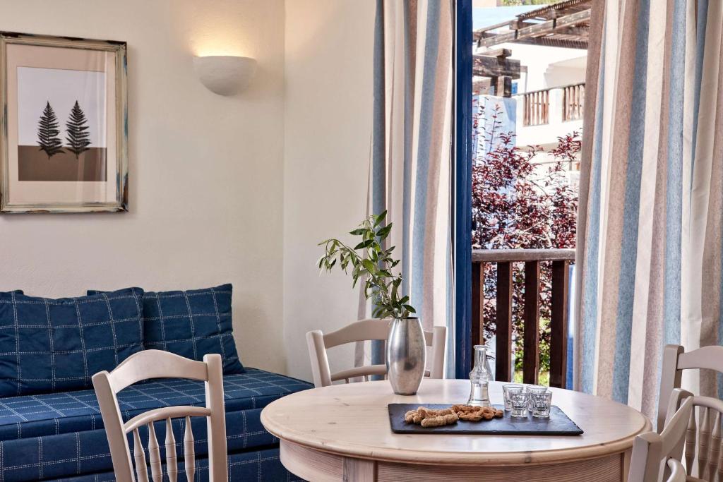 Mūsdienīgs interjers ar zilu dīvānu, koka galdu un ērtām krēsliem, kurā redzams ziedu pušķis un cepumi uz galda. Logā ir gaisīgas svītrainas aizkaru, kas piedod telpai gaisīgumu.