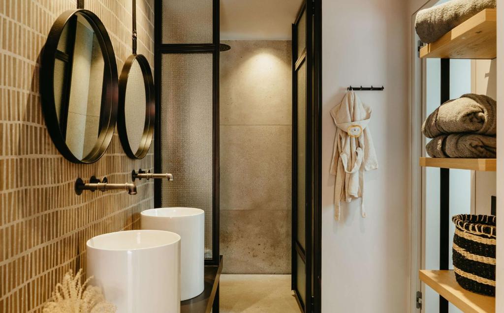 Mūsdienīgs vannas istabas interjers ar divām apaļām spoguļiem, baltām izlietnēm un siltām tekstilmateriālu akcentiem. Detalizēts dizains, kas apvieno eleganci un funkcionalitāti.