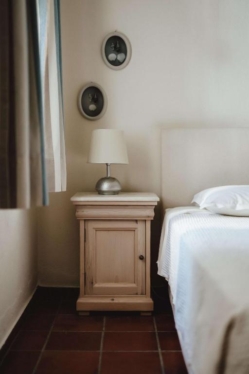 Mūsdienīgs guļamistabas stūris ar koka naktsgaldiņu un lampu, blakus gultai ar baltu gultasveļu. Sienā redzami divi apļveida attēli.