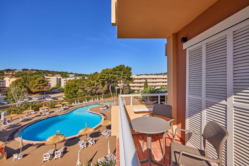 Skats no balkona uz baseinu un apkārtējo ainavu, kur redzami sauļošanās krēsli un zaļi koki. Ideāla vieta atpūtai un relaksācijai.