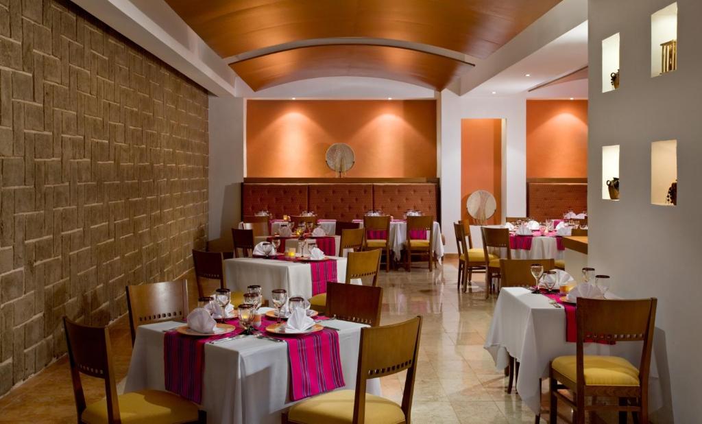 Elegantas restorāna interjers ar galdiem, kas klāti ar baltām galdautām un krāsainām dekorācijām. Siltas krāsas sienās un apgaismojumā rada patīkamu atmosfēru.