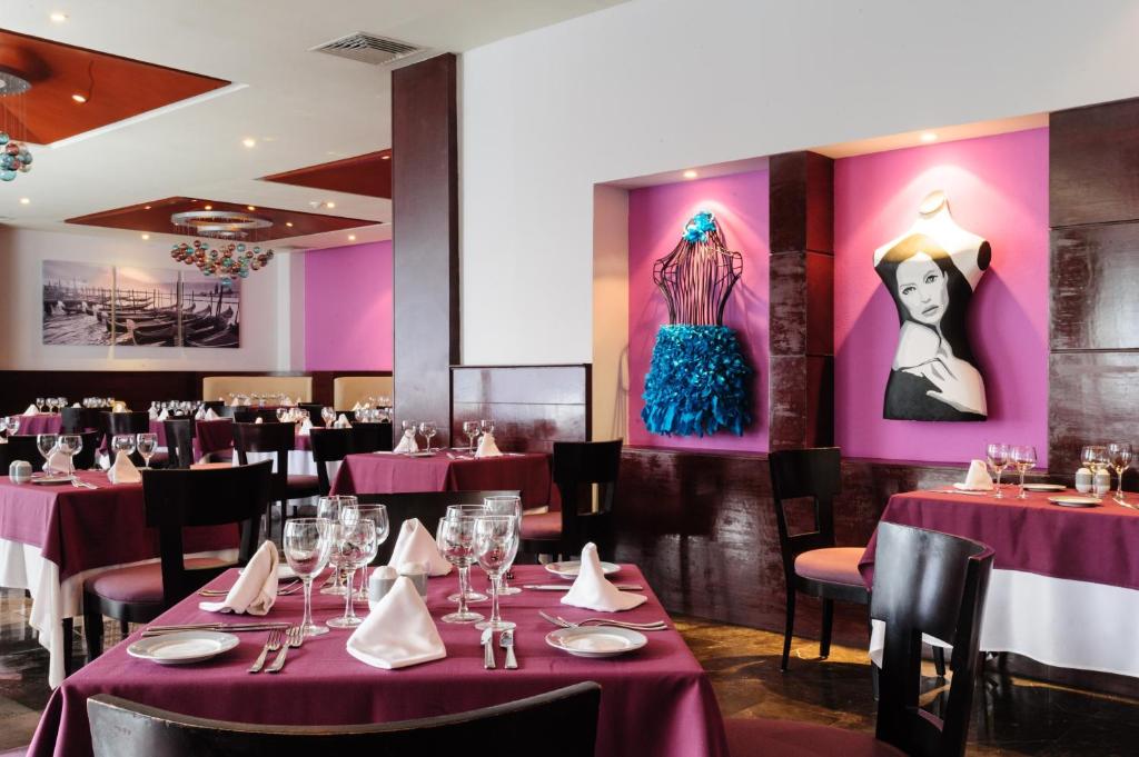 Mūsdienīgs restorāns ar elegantu interjeru, kurā ir sarkanas un violetas krāsas akcenti, kā arī mākslinieciskas dekorācijas uz sienām. Galdi ir uzklāti ar baltiem galdautiem un stikla traukiem, radot patīkamu atmosfēru.